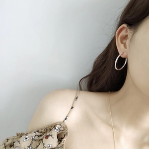Close-up of minimalist sterling silver Mobius hoop earrings worn by a model in a natural setting