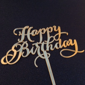 Macro shot of mirror gold acrylic cake topper with elegant Happy Birthday lettering
