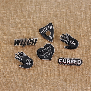 Detail of 6 black enamel pins featuring WITCH, CURSED and OUIJA mystical symbols on fabric