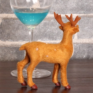 Lifelike brown flocked Christmas reindeer ornament with white spots on dark wood surface