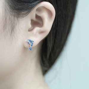 Close-up of a model wearing a small blue and white dolphin stud earring with pave stones