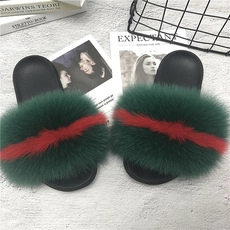Top view of green faux fur slippers with red stripes on a textured grey background