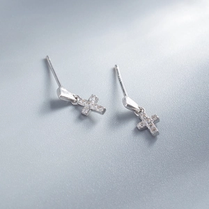Macro shot of silver cross earrings with clear zircon stones on a grey background