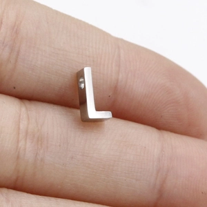 Macro shot of a tiny silver stainless steel L-shaped pendant tag held on a finger for scale