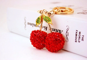 Macro shot of red rhinestone cherry keychain with green leaves on golden plating