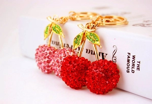 Close-up of red and pink cherry keychains with sparkling rhinestones on a book