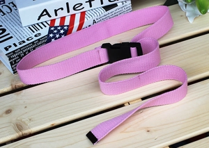 Pink canvas belt with black plastic buckle detail shown on a light wooden background