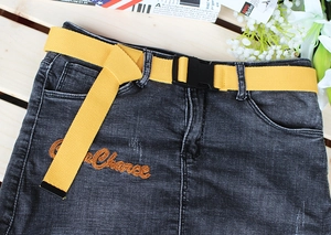 Close-up of a black denim skirt featuring a bright yellow canvas belt with plastic buckle