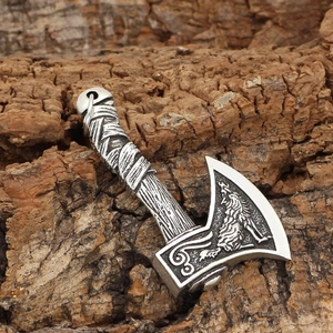 Close-up of Viking double-sided axe pendant with wolf relief on textured wood surface