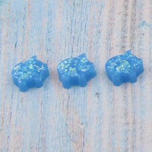 Three cute blue synthetic opal pig pendants for DIY jewelry making on wood background