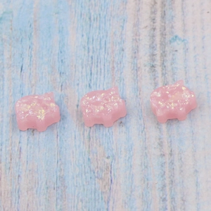 Three cute pink glitter resin pig charms for DIY jewelry making on wood surface