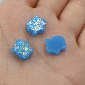 Detailed view of three blue pig-shaped opal beads held in hand for scale and texture
