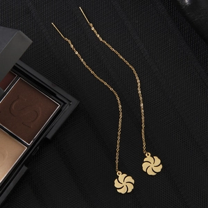 Macro view of gold flower pendant earrings with long delicate chain tassels on dark mesh