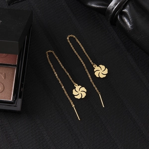 Close-up of golden windmill flower threader earrings on textured black leather surface