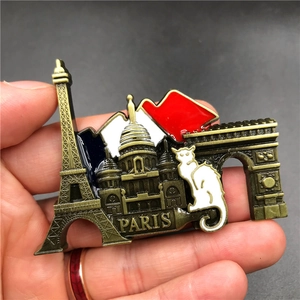 Detailed close-up of a bronze Paris souvenir fridge magnet held by hand for scale