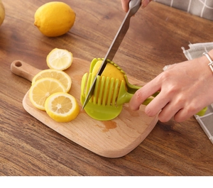 Close-up of green manual lemon slicer holder being used on a wooden cutting board