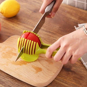 Handheld green tomato and lemon slicer guide tool on a wooden cutting board