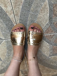 Detail showing gold and silver heart anklets on woman's ankle with studded sandals