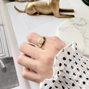Golden signet ring with etched sun and eye pattern worn against a vintage book background