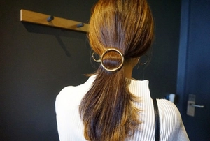 Close-up of a minimalist golden circular metal hair clip securing a ponytail hairstyle