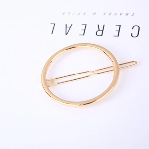 Detail of minimalist golden circular metal hair clip with polished finish on white background