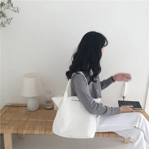 Detail of white canvas tote bag with black mercipa letter print and wide strap