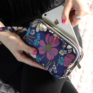 Three-layer floral fabric wallet with wristlet strap holding a smartphone