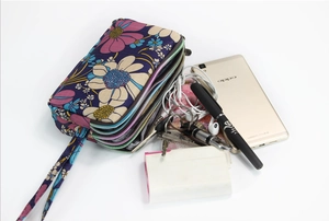 Detail of floral canvas wristlet with three zipper pockets holding phone and accessories