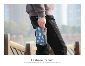 Three-layer blue floral fabric wallet with wrist strap held outdoors by a model