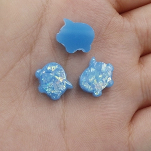 Macro shot of three blue pig-shaped synthetic opal beads held on a palm for DIY jewelry