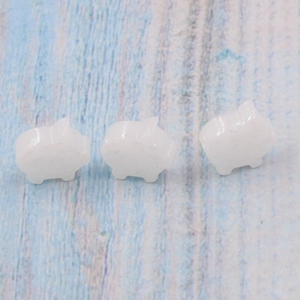 Three cute pig-shaped white opal stone beads for DIY jewelry on blue wood background
