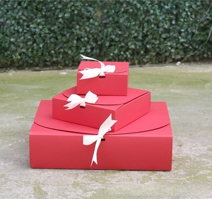 Three sizes of red gift boxes with white ribbon bows stacked in an outdoor setting