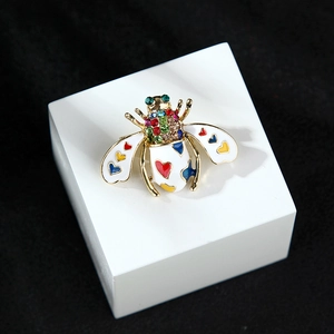 Golden bee brooch with white enamel wings and colorful rhinestones on a black background
