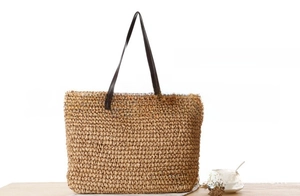 Detail view of straw tote bag with brown leather handles and beige floral accessory