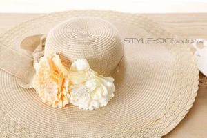 Detail of straw sun hat featuring orange and white artificial flowers and polka dot ribbon