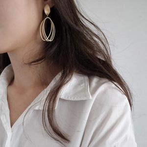 Minimalist matte gold geometric oval drop earrings on a model wearing a white shirt