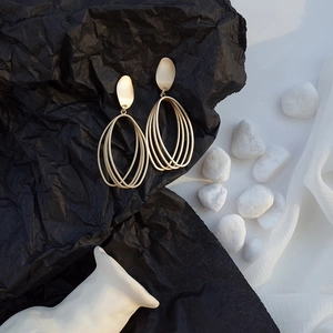 Close-up of matte gold geometric multi-layer oval drop earrings on artistic background
