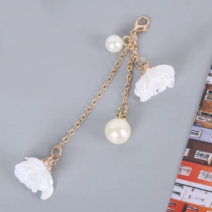 Detail view of multi-layer golden phone charm with white pearls and fabric floral pendants
