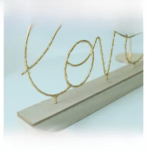 Detailansicht des goldenen Eisen-Love-Schriftzugs und des Holzsockels mit LED-Drahtlichtern