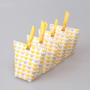 Set of four paper gift bags with tulip patterns and yellow ribbon handles on grey background