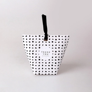 Close-up of a white gift box with black polka dots and a black silk ribbon handle