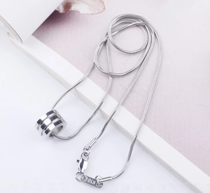 Macro detail of silver snake chain necklace and cylindrical pendant with K18 engraving