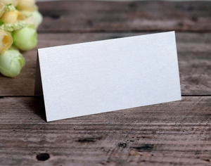 Detail of white pearlescent place card with glitter texture on a rustic wooden table