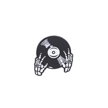Detail of metal skull hands holding a vinyl record enamel pin on a white background