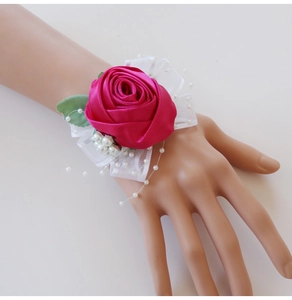 Close-up of rose wrist corsage with magenta silk flower, white lace, and pearl details