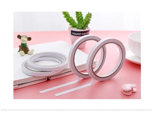 Double-sided white adhesive tape rolls for office and DIY on a pink desk background