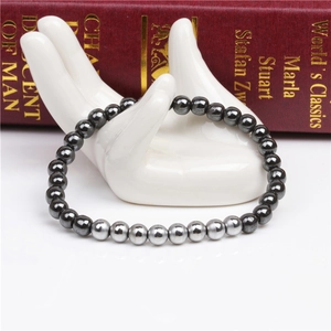 Close-up of 6mm magnetic hematite beads on a white ceramic hand display with vintage book