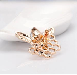 Macro view showing the detailed golden metal bee atop an intricate hollow honeycomb brooch