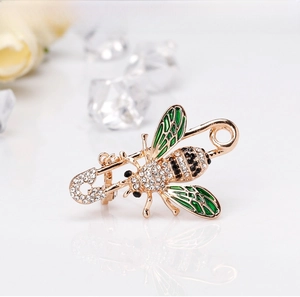 Detailed close-up of a gold bee brooch featuring green enamel wings and clear crystals