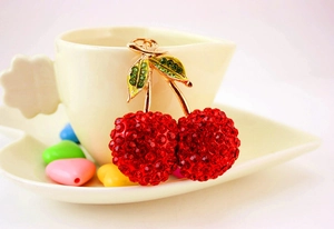 Macro shot of cherry keychain with red and green rhinestones on a ceramic cup rim